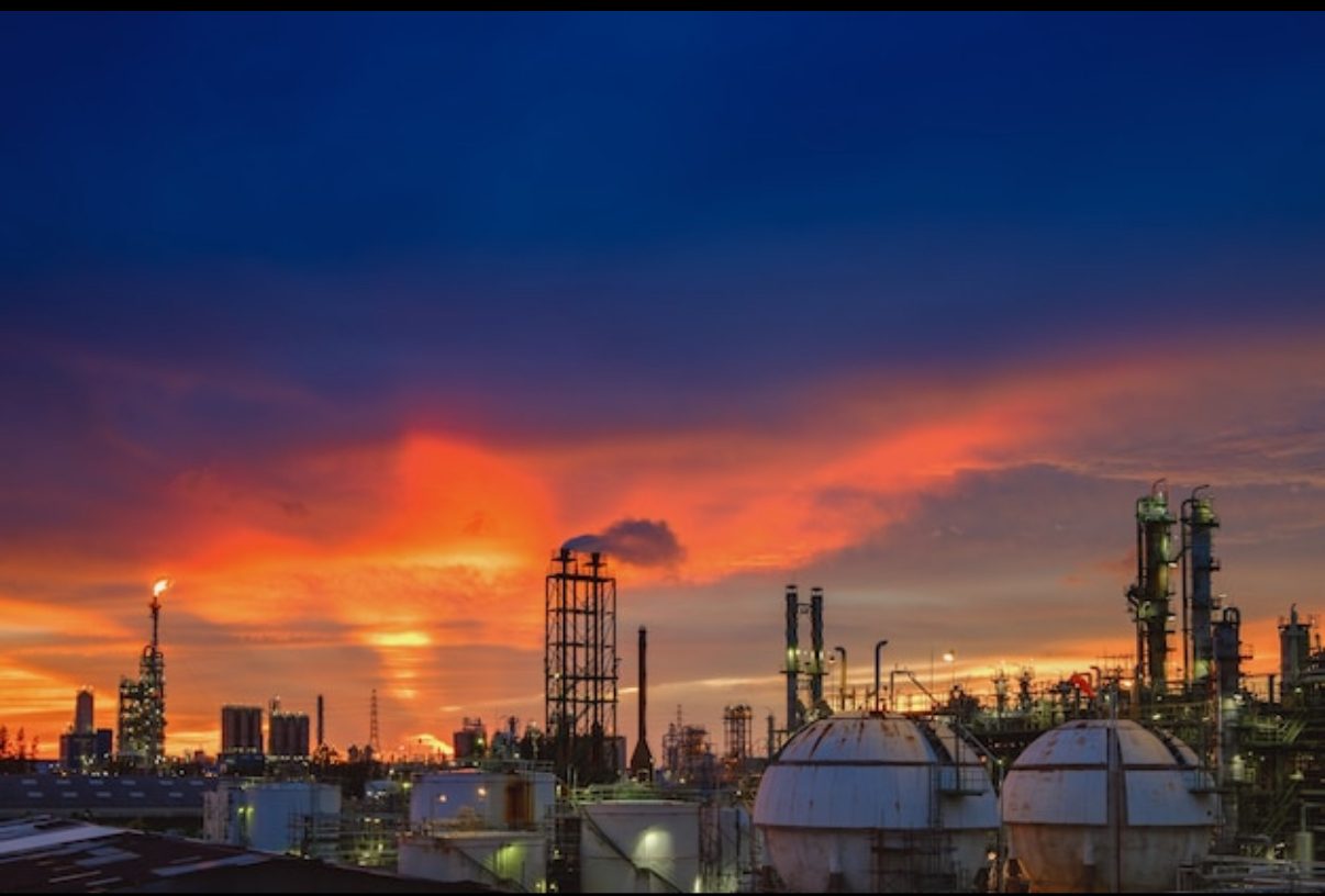 Industrial refinery at sunset with stacks, columns and storage spheres in silhouette
